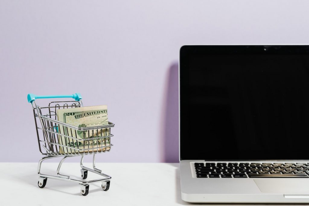 laptop and a small shopping cart with paper bills